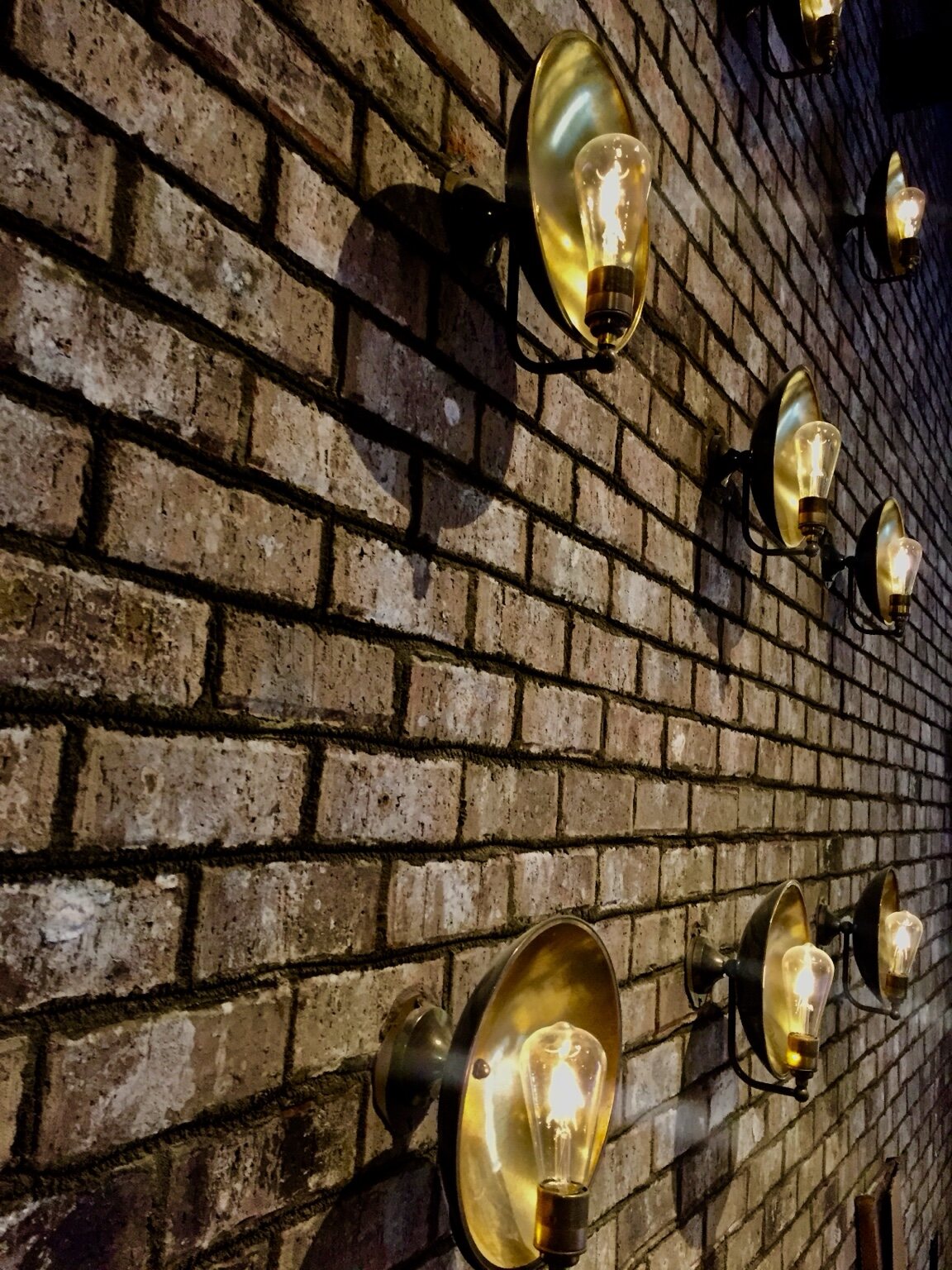 Brass wall lights arranged across textured brick at Coalition Food and Beverage