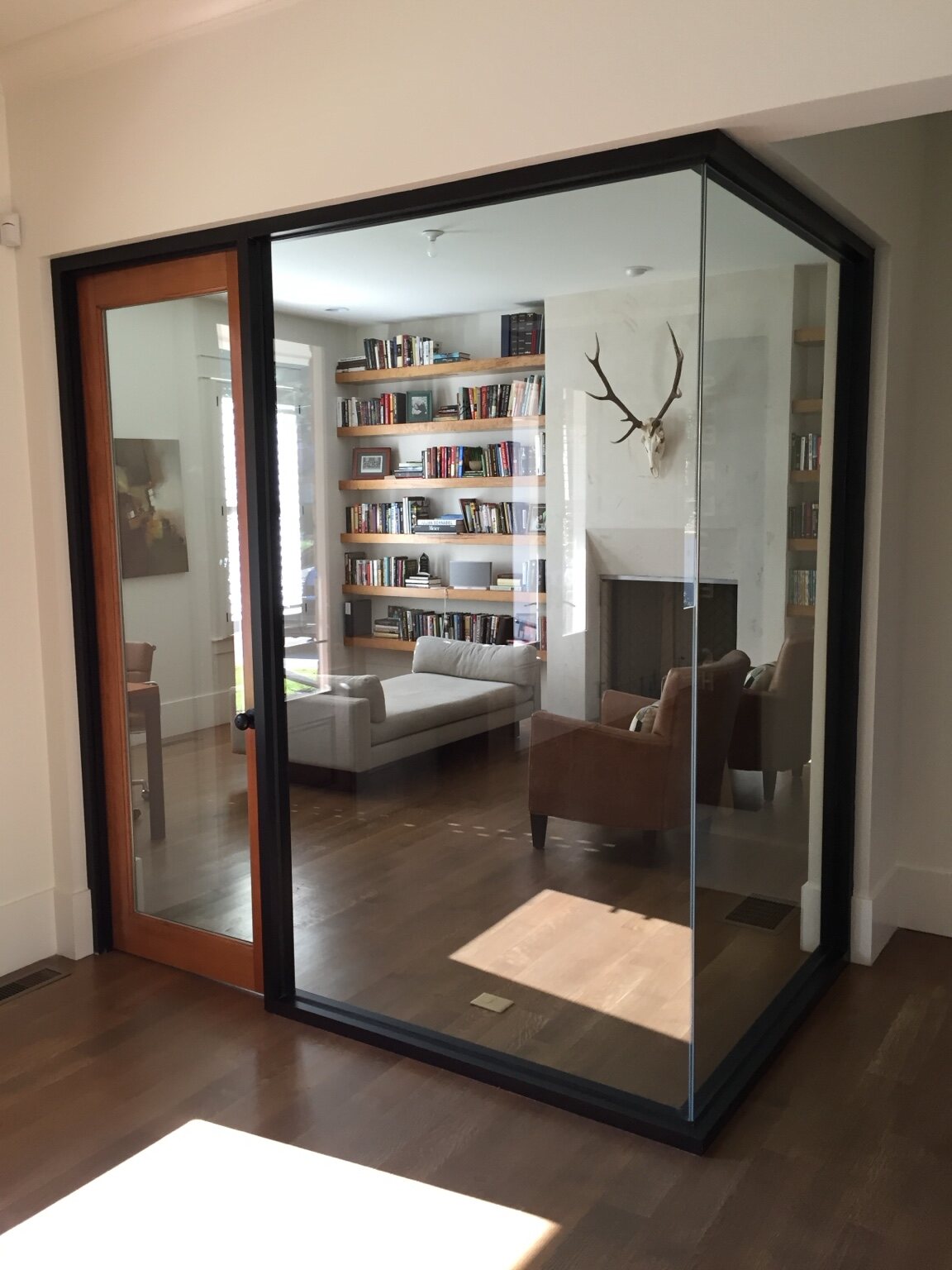 Glass-enclosed study with floating wood shelves and a stone fireplace